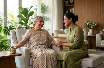 Indian caregiver holding hands and talking with a smiling elderly woman in a comfortable living room, showcasing compassionate senior care, companionship, and emotional support at home.